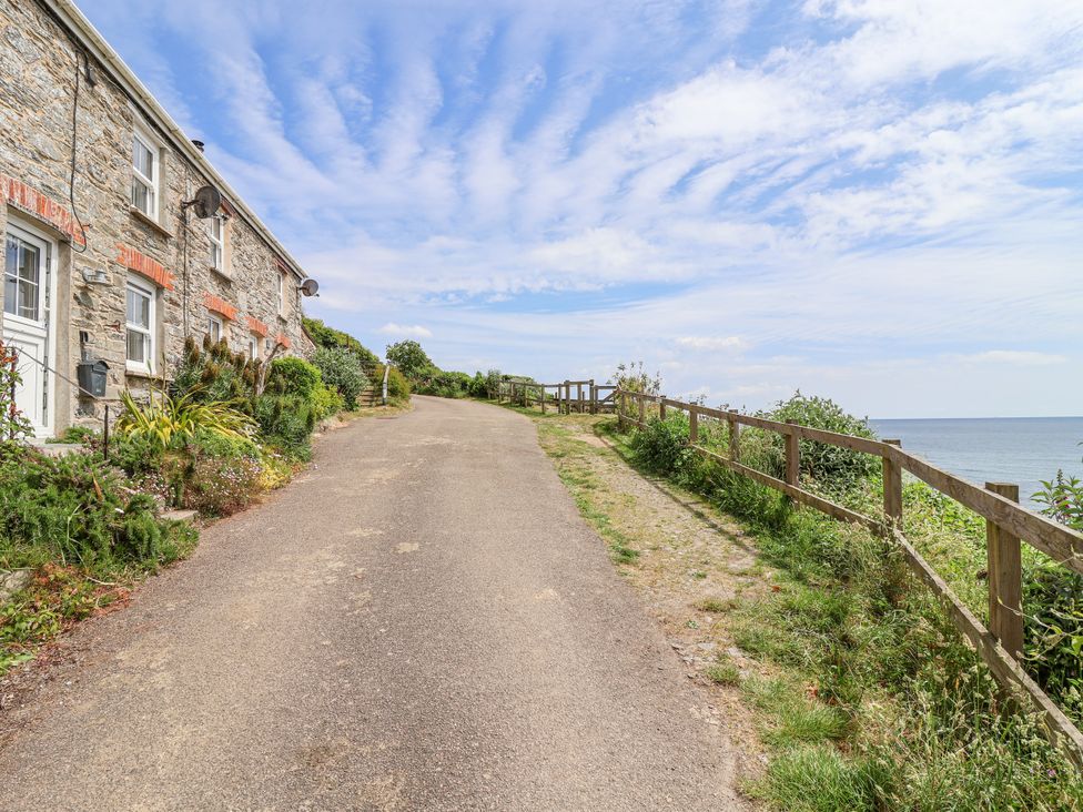 A pathway beside a stone house leading to the ocean at 2 Cliff Cottages West Portholland near Gorran Haven