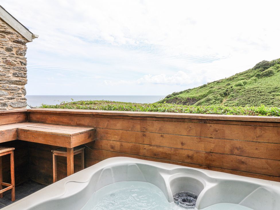 An outdoor area with a hot tub and wooden seating overlooking the ocean at 2 Cliff Cottages West Portholland near Gorran Haven