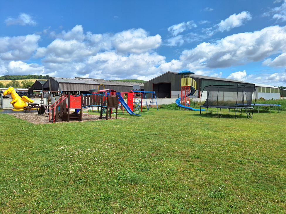 An outdoor play area with a slide, swings, and trampoline at Farm Yard Cottage, Allerston