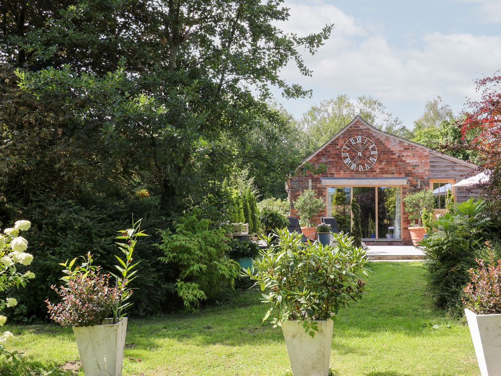 A garden with plants and a building featuring a clock at Ladycroft Barn in Ashbourne