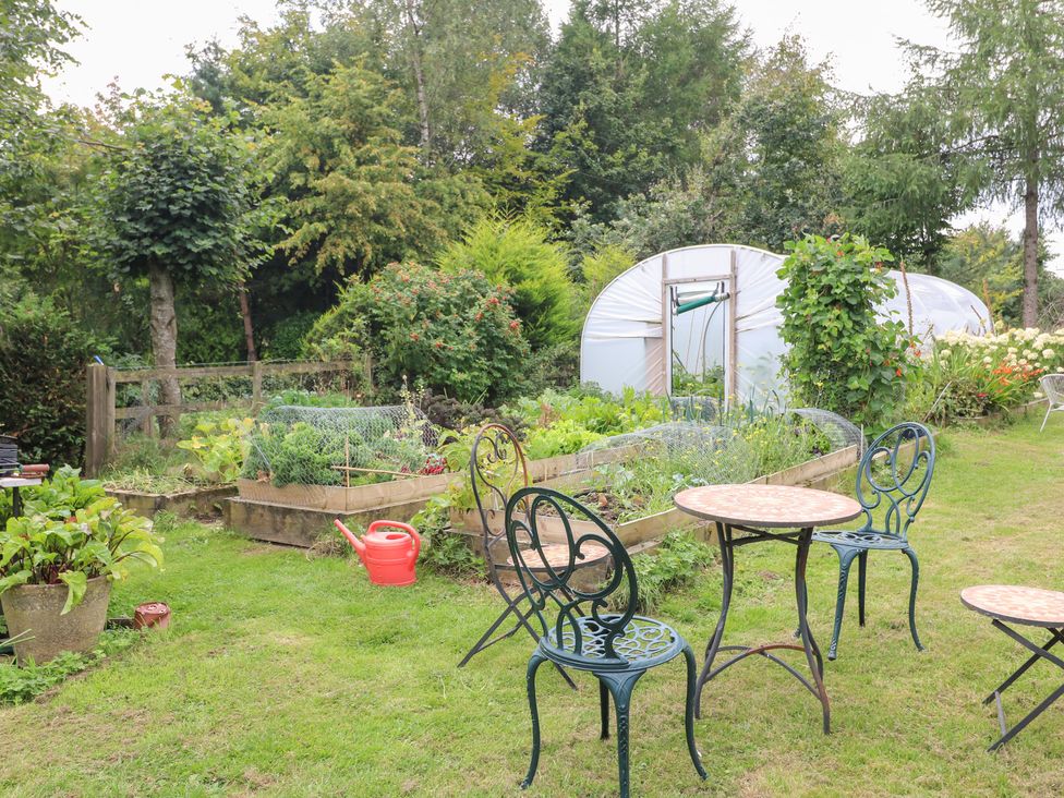 A garden with plants, table, chairs and a greenhouse at Ladycroft Barn in Ashbourne