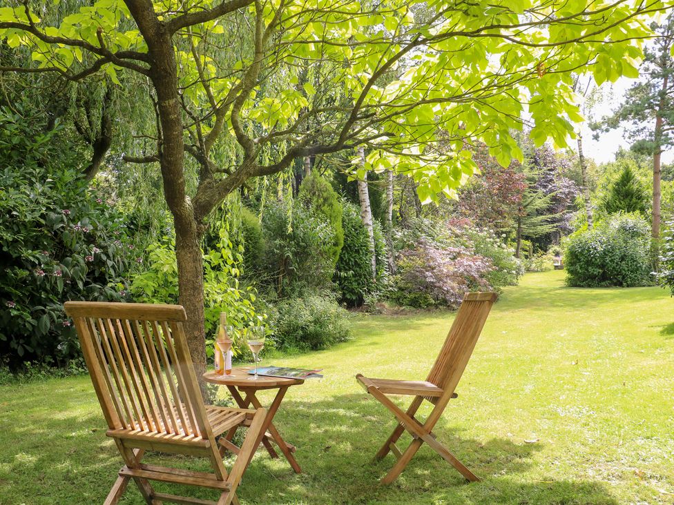 A garden with wooden chairs and a table under a tree at Ladycroft Barn Ashbourne