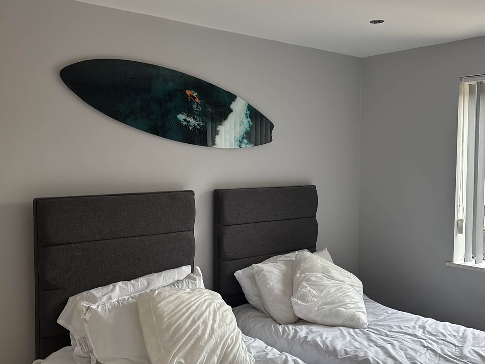 A bedroom with two beds and a surfboard on the wall at Fistral Apres Surf in Newquay