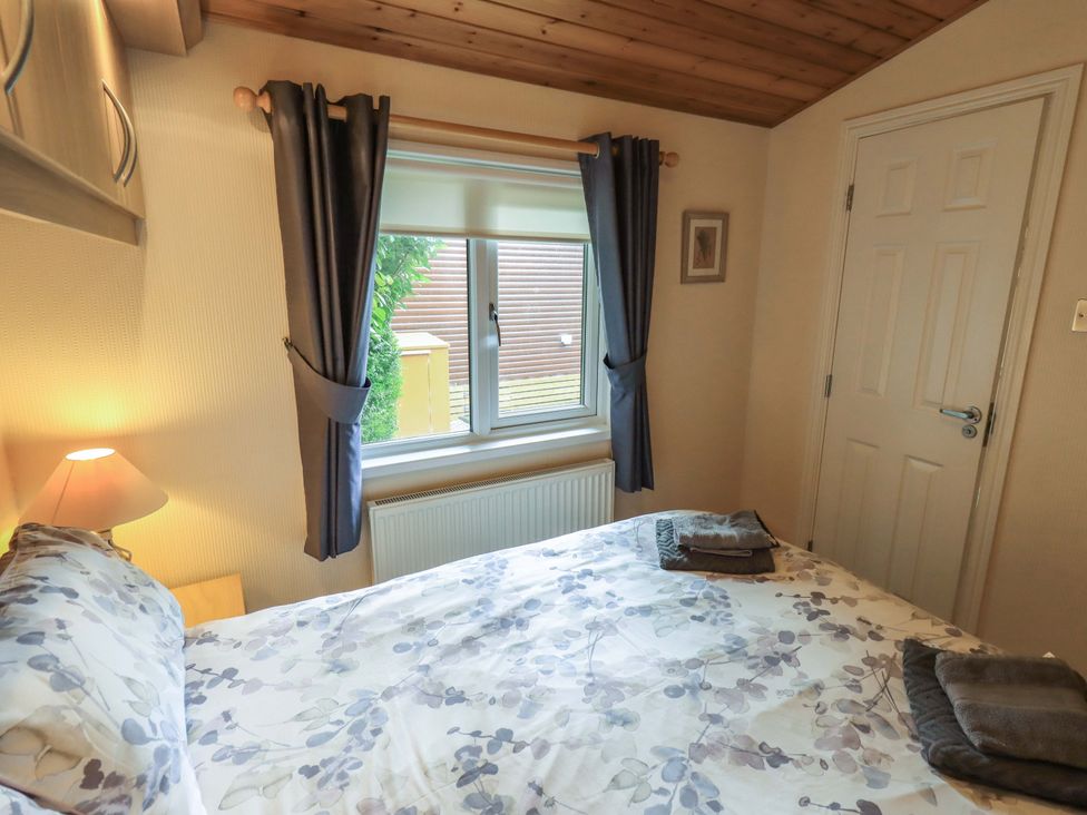A bedroom with a bed, lamp, and window at Birthwaite Lodge, Fellside 6, Limefitt Park near Windermere