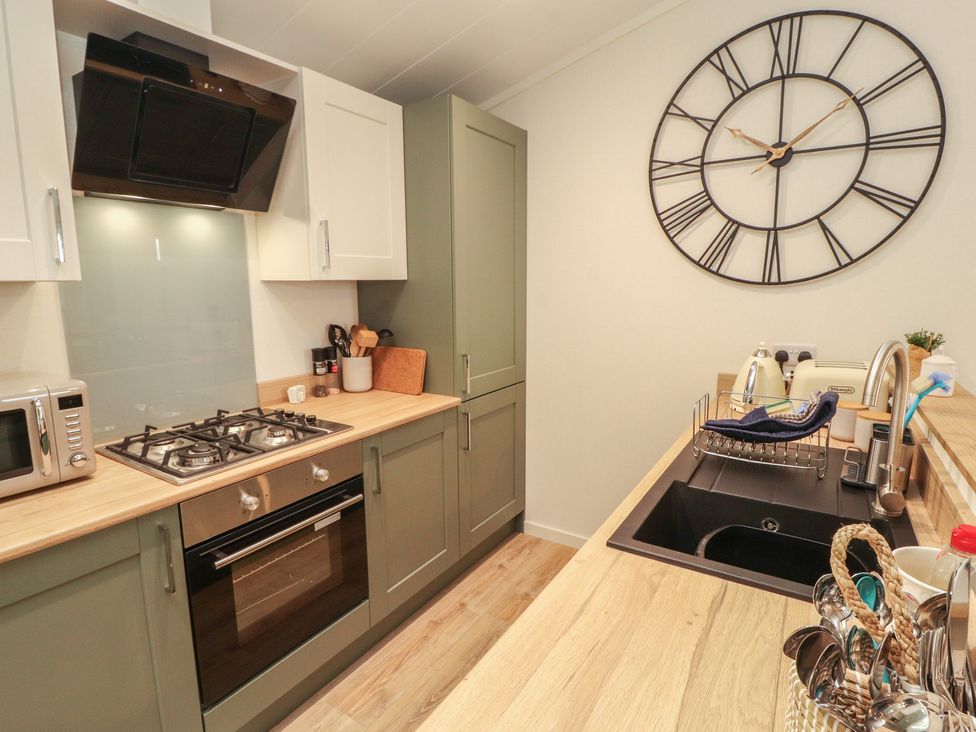 A kitchen with cabinets, cooker, sink, and clock at Beech Grove Lodge, Glade 17, Fallbarrow Park near Bowness on Windermere