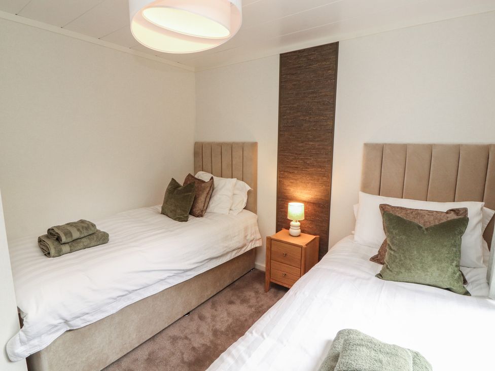 A bedroom with two beds and a bedside table at Beech Grove Lodge, Glade 17, Fallbarrow Park near Bowness on Windermere
