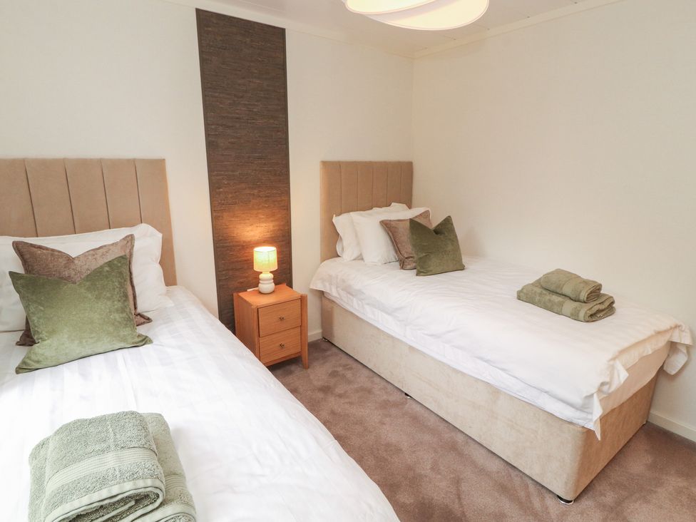 A bedroom with two single beds and a nightstand at Beech Grove Lodge, Glade 17, Fallbarrow Park near Bowness on Windermere