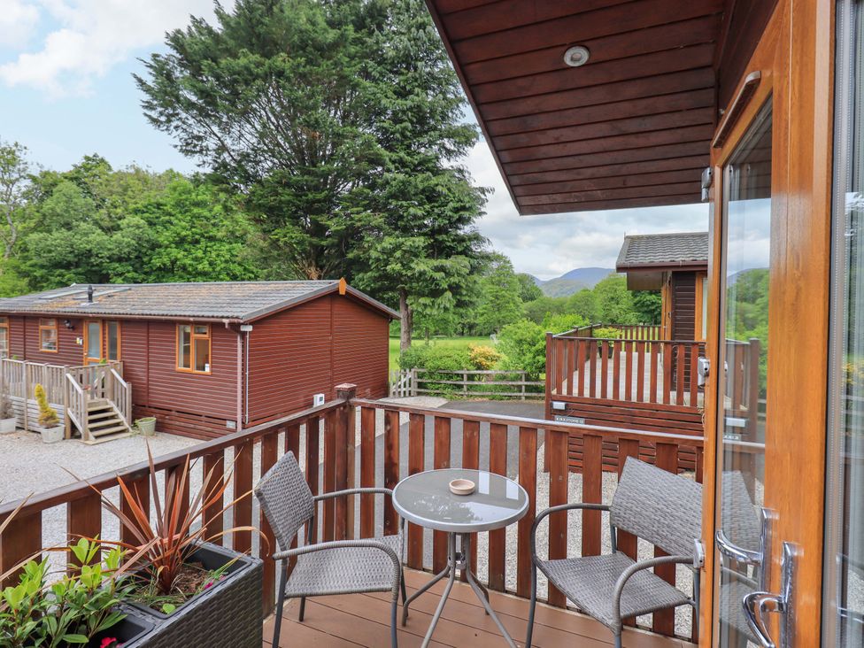 A small balcony with two chairs and a round table overlooking wooden cabins and trees at Pheasant's Nest Kirkstone 11 Limefitt Park near Windermere