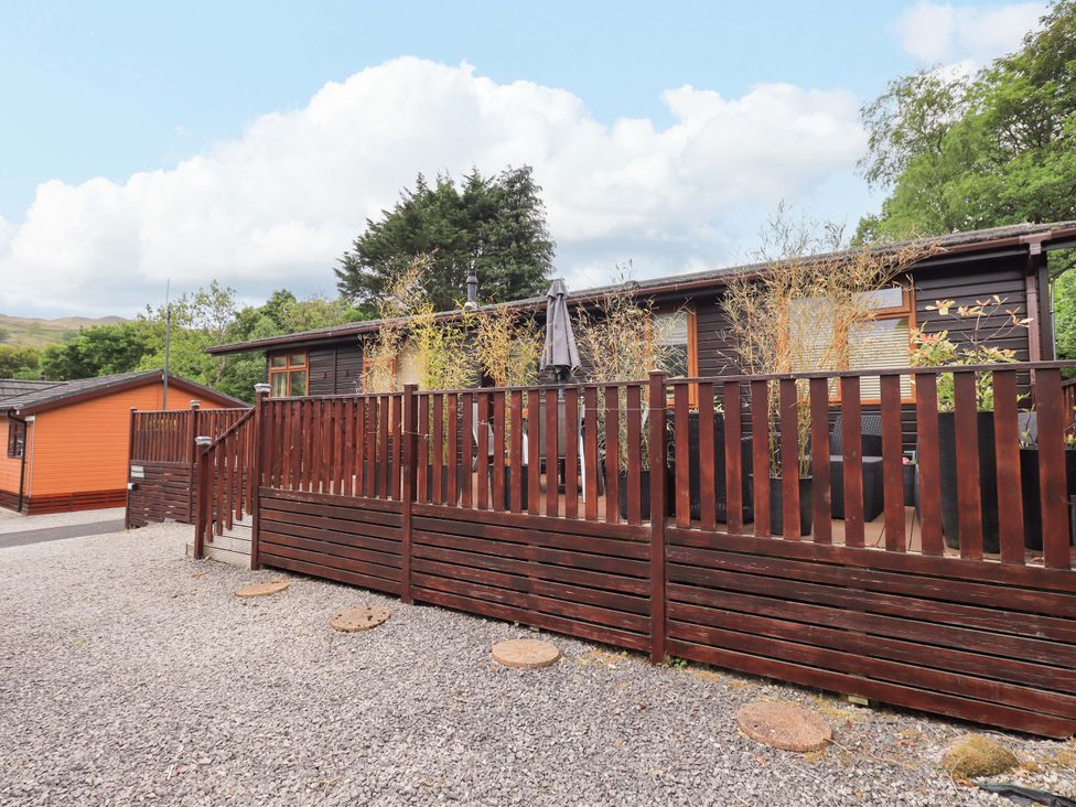 A wooden deck with potted plants and an umbrella fenced by wooden railings outside a dark wooden cabin at Pheasant's Nest in Kirkstone 11 Limefitt Park near Windermere