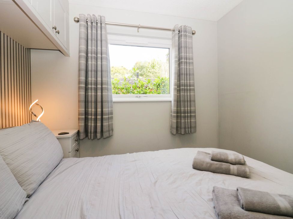 A bedroom with a bed, curtains, and a lamp at Badgers Hollow Lodge Grasmere 30, White Cross Bay near Windermere