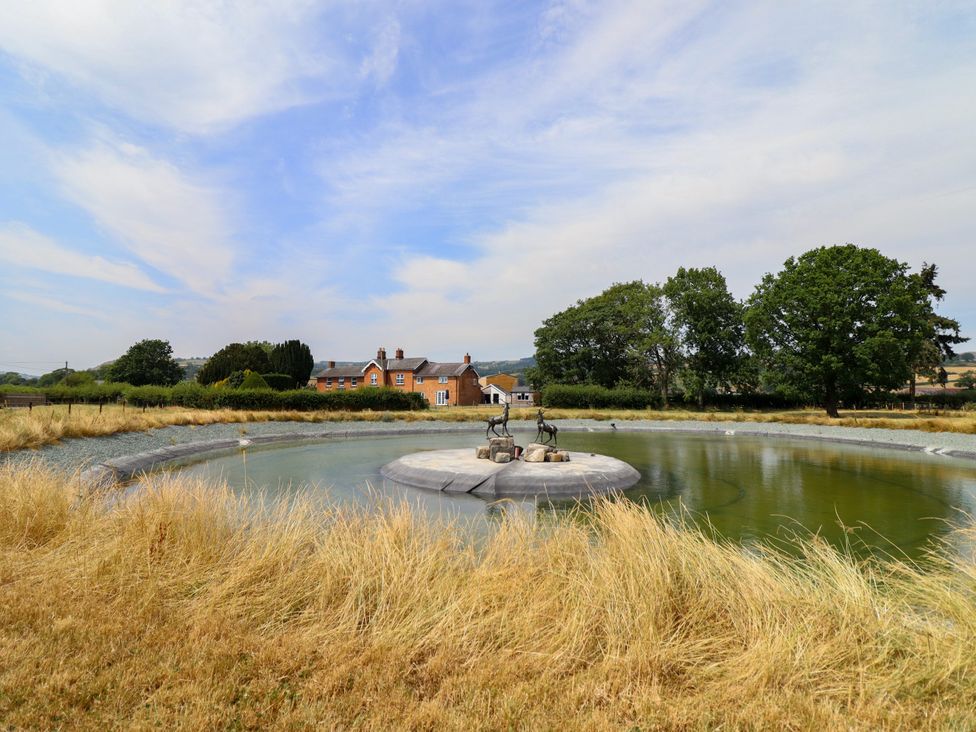 A fountain surrounded by grass and a house in the background at Bodaioch Hall Trefeglwys near Caersws