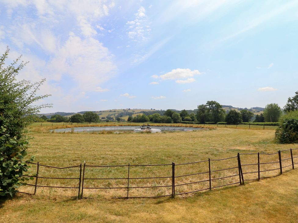A view of a pond surrounded by grass field and hills at Bodaioch Hall Trefeglwys near Caersws