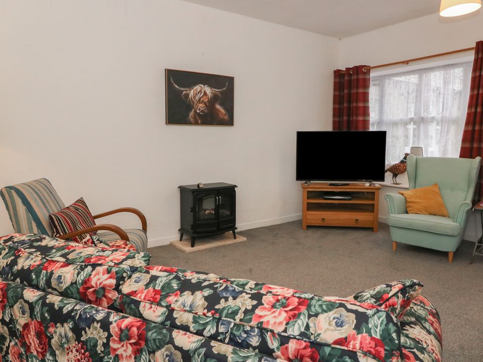 A living room with a sofa, armchair, TV, and fireplace at Holly Cottage near Killean Farmhouse Cottages near Inveraray