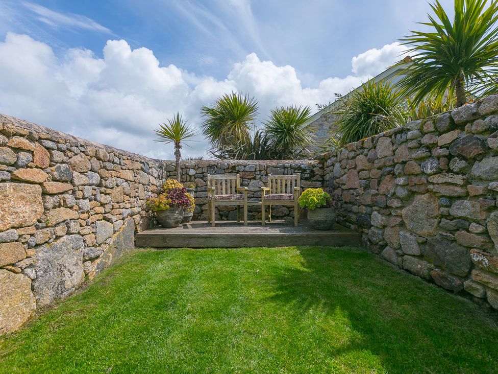 A garden with a stone wall and wooden benches at Scilly Stack in Penzance