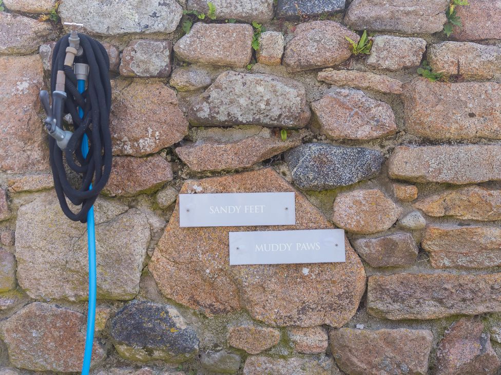 A hose and signs labeled 'SANDY FEET' and 'MUDDY PAWS' on a stone wall at Scilly Stack in Penzance