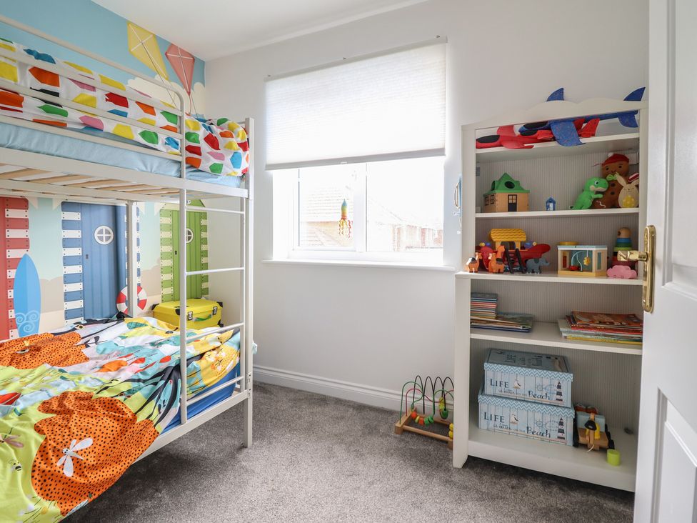 A children's bedroom with a bunk bed and a shelf full of toys at The Beach House in Prestatyn