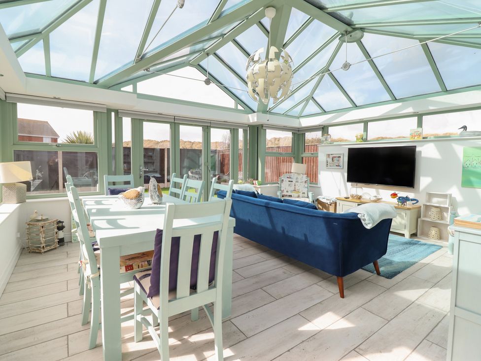 A conservatory with a dining table and sofas at The Beach House in Prestatyn