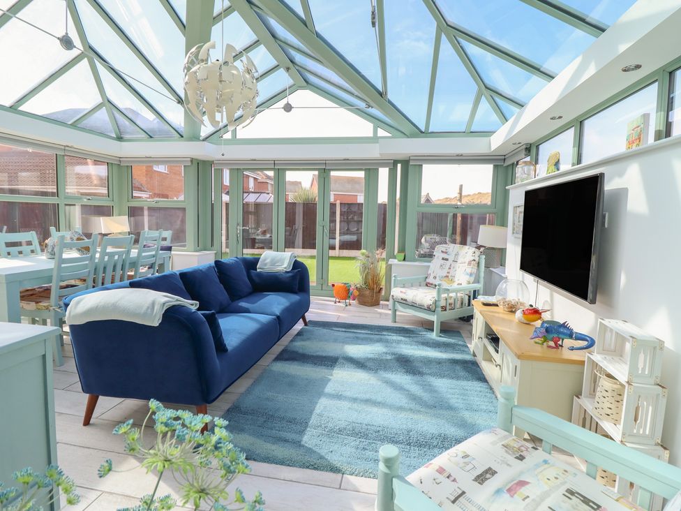 A conservatory with a sofa, dining table, and television at The Beach House in Prestatyn
