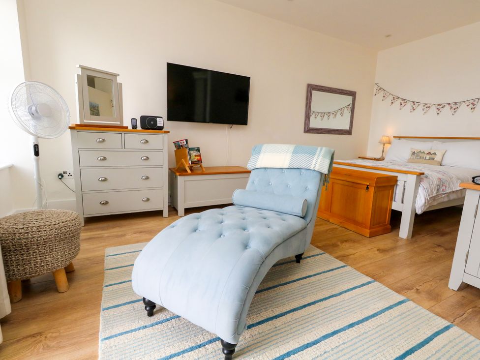 A bedroom with a chaise lounge and television at 4 The Beaches in Weymouth