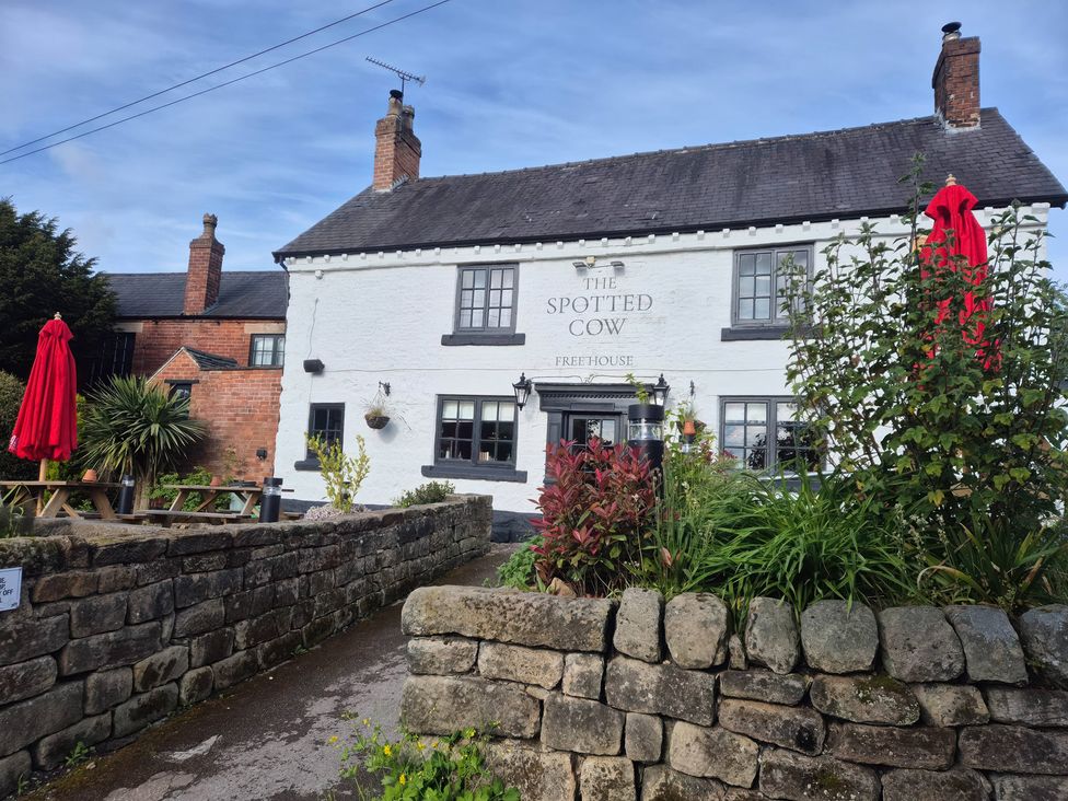 A pub with a stone wall and red umbrellas at The Spotted Cow in Holbrook, Derbyshire