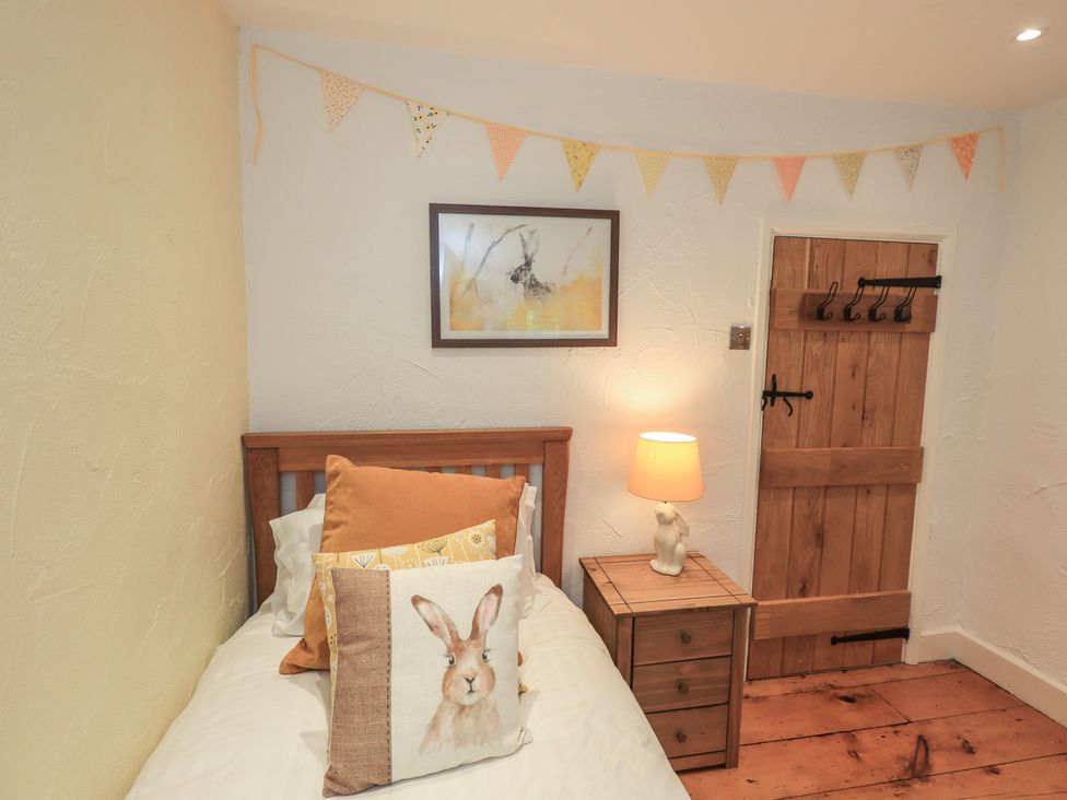 A bedroom with a bed, side table, lamp and decorations at Green Stile Cottage in Bowness-On-Windermere