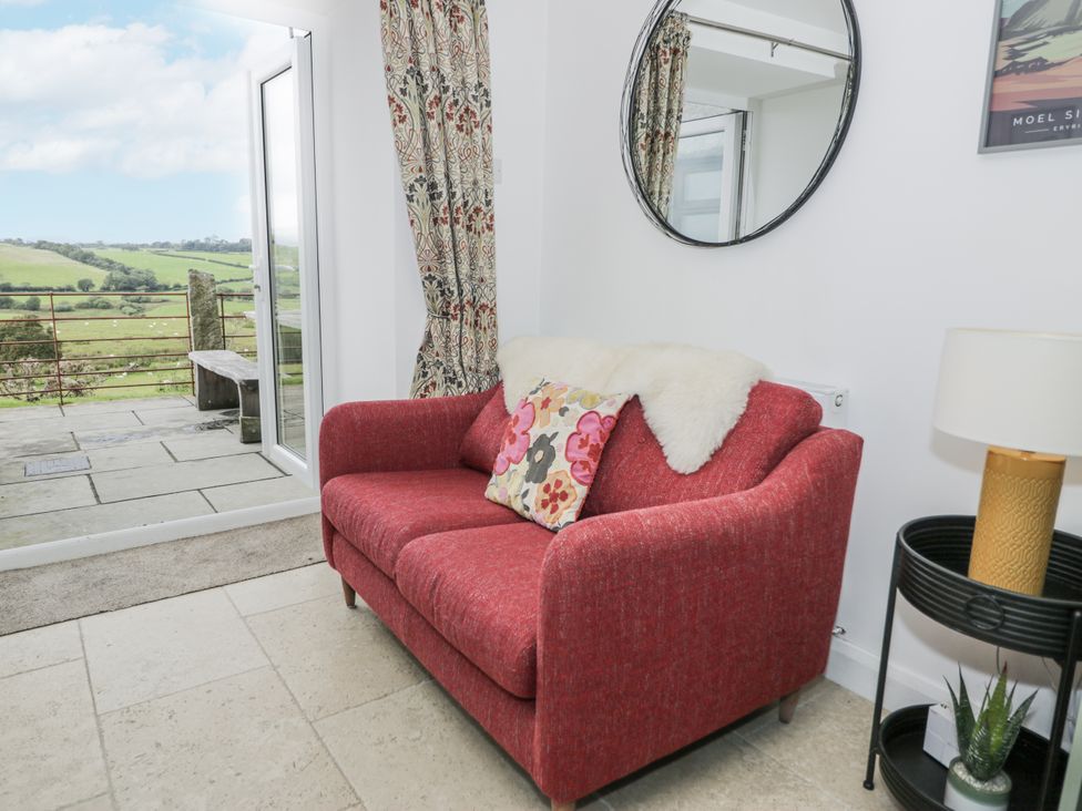 A living room with a red sofa and a view of the outdoors at Orsedd Wen Farmhouse in Betws-Y-Coed
