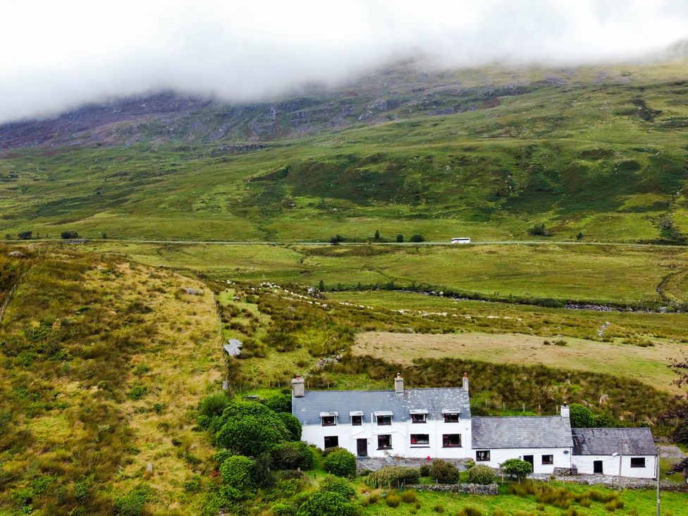 A house in a grassy area with mountains and clouds at Cwm Capel Curig