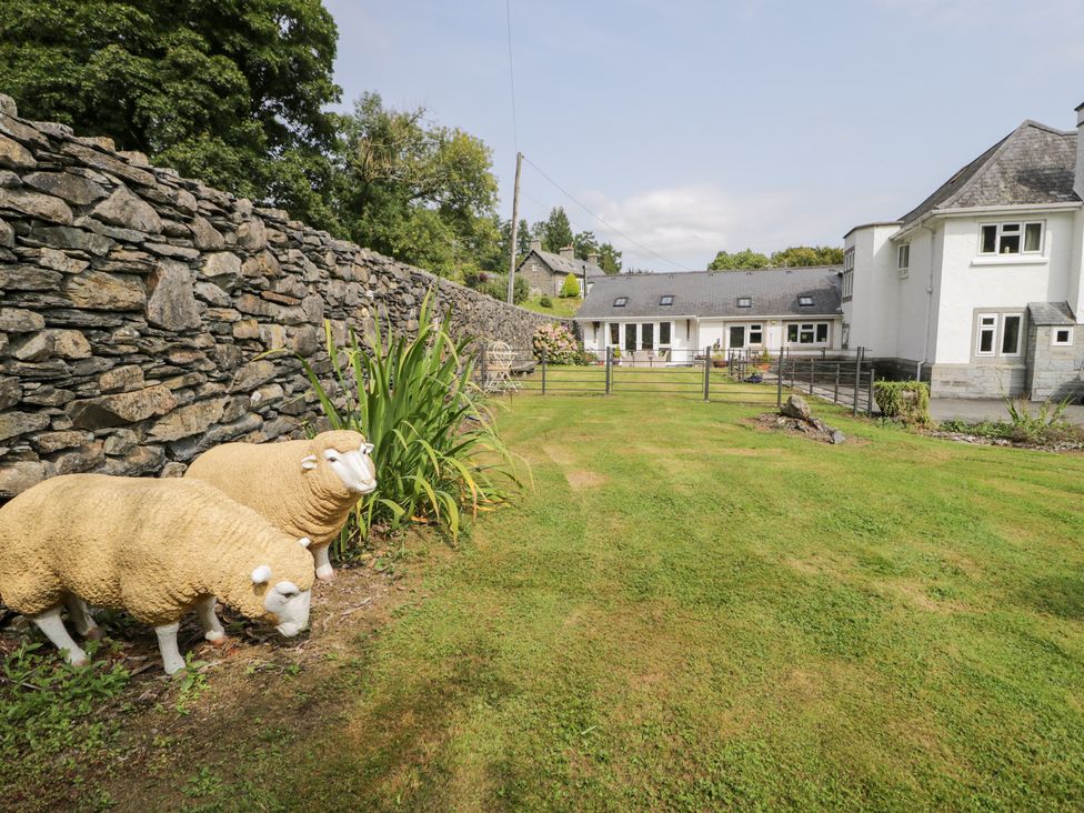 A garden with sheep sculptures and a stone wall at Pengwern Bach Llanrwst