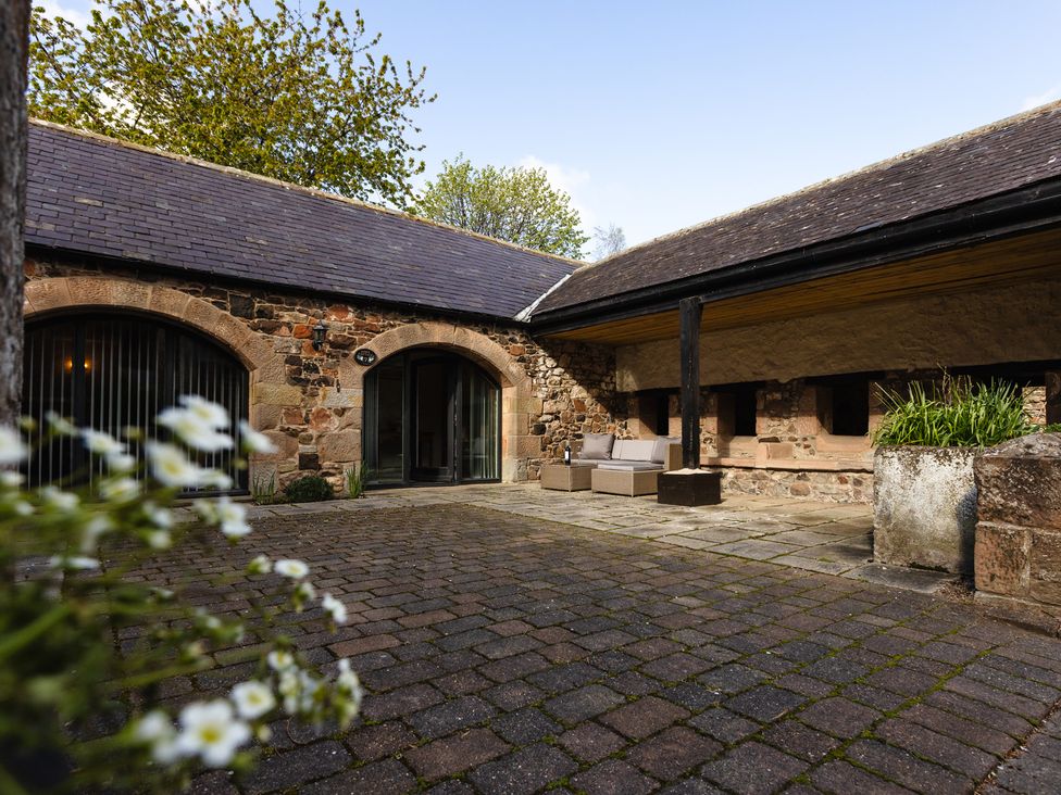 An outdoor area with stone walls and lounge furniture at Fern Cottage in Akeld near Wooler