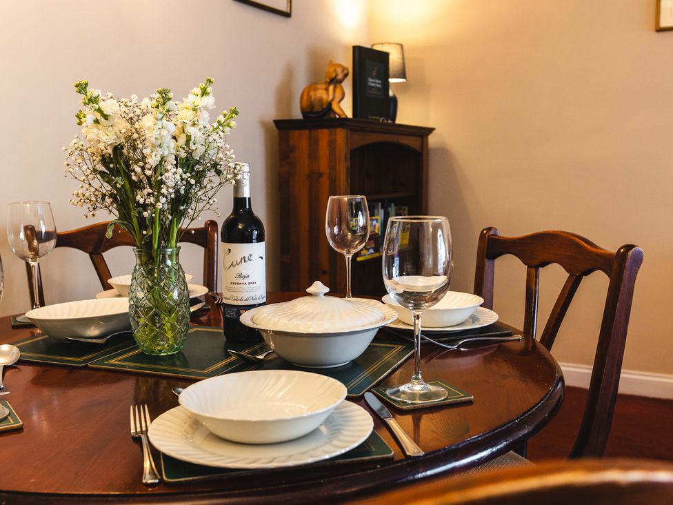 A dining table set with plates, glasses, and a wine bottle at Fern Cottage in Akeld near Wooler
