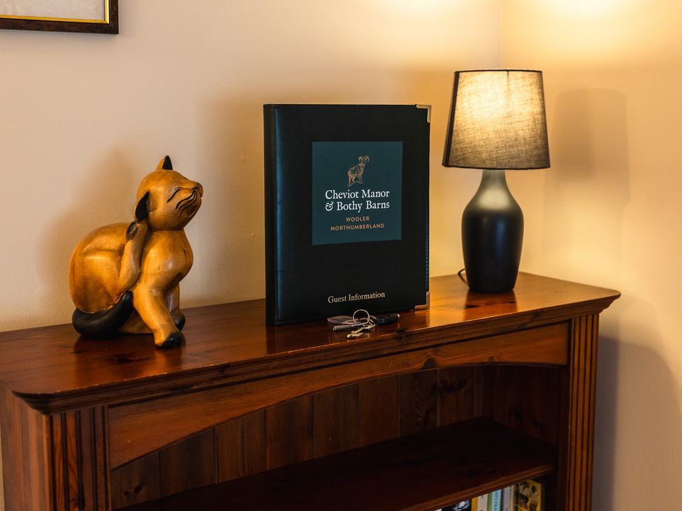 A wooden cabinet with a cat statue and guest information booklet at Cheviot Manor in Wooler