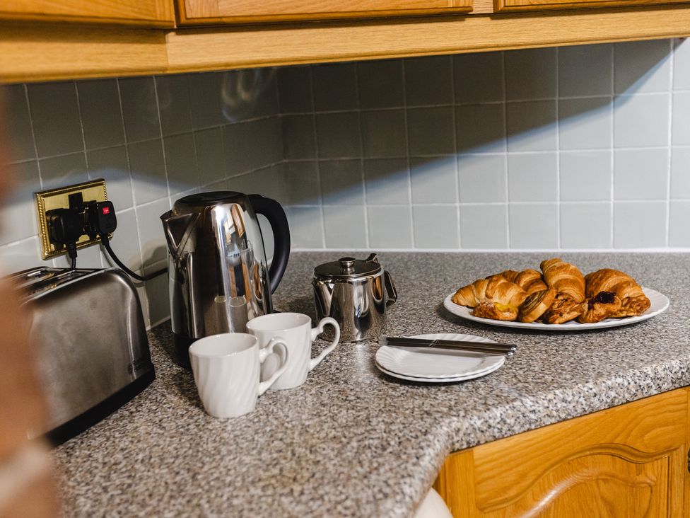A kitchen counter with a kettle, toaster, mugs, teapot, and croissants at Fern Cottage in Akeld near Wooler
