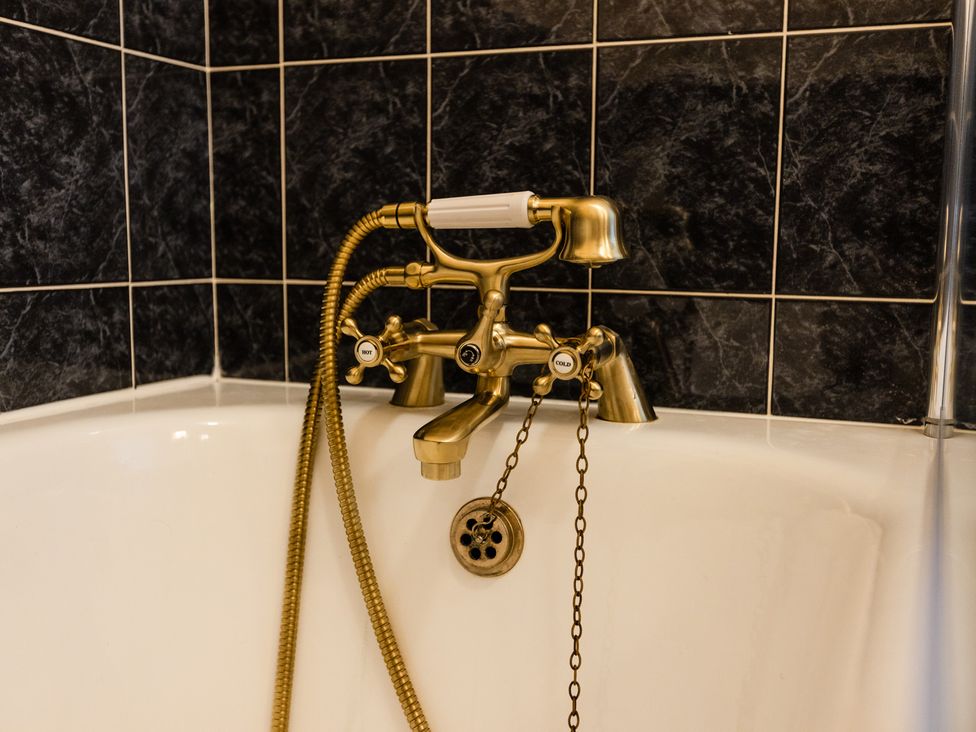 A bathtub with a gold faucet and shower head at Fern Cottage in Akeld near Wooler