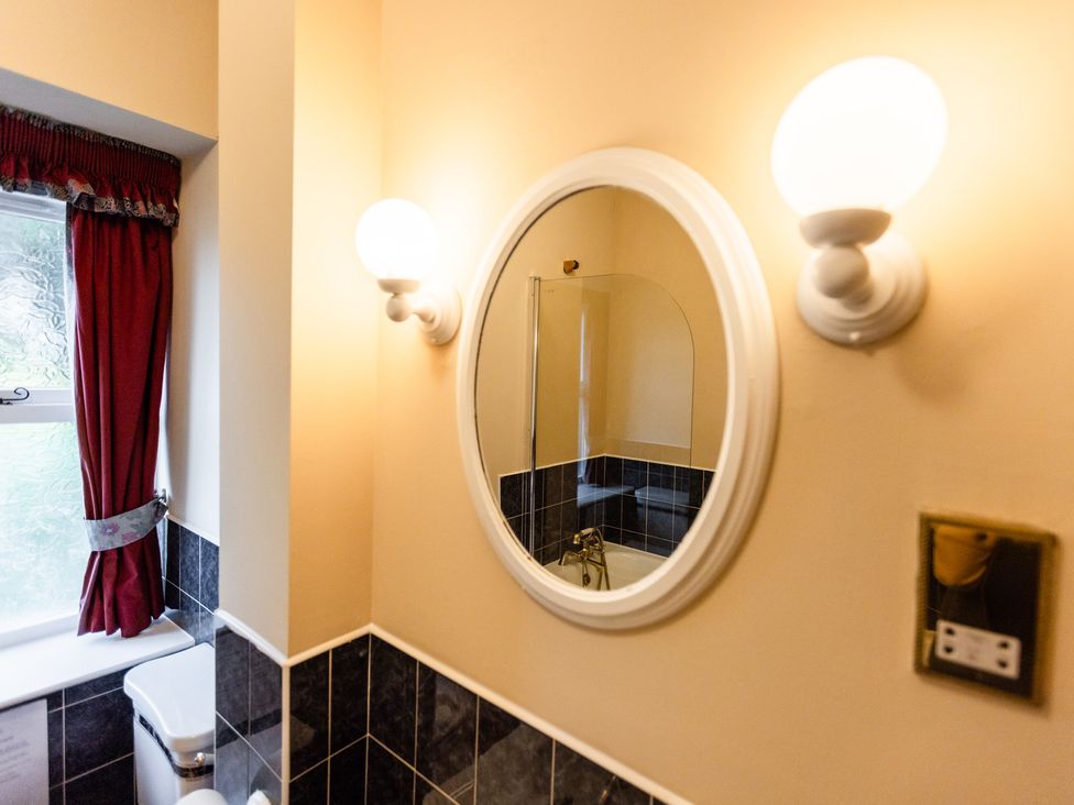 A bathroom with a mirror, toilet and light fixtures at Fern Cottage in Akeld near Wooler