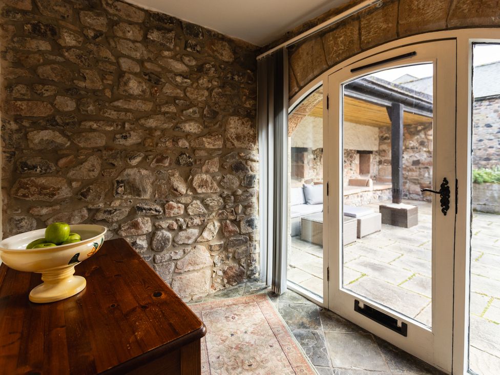 A room with a stone wall and a door leading to an outdoor patio at Fern Cottage in Akeld near Wooler