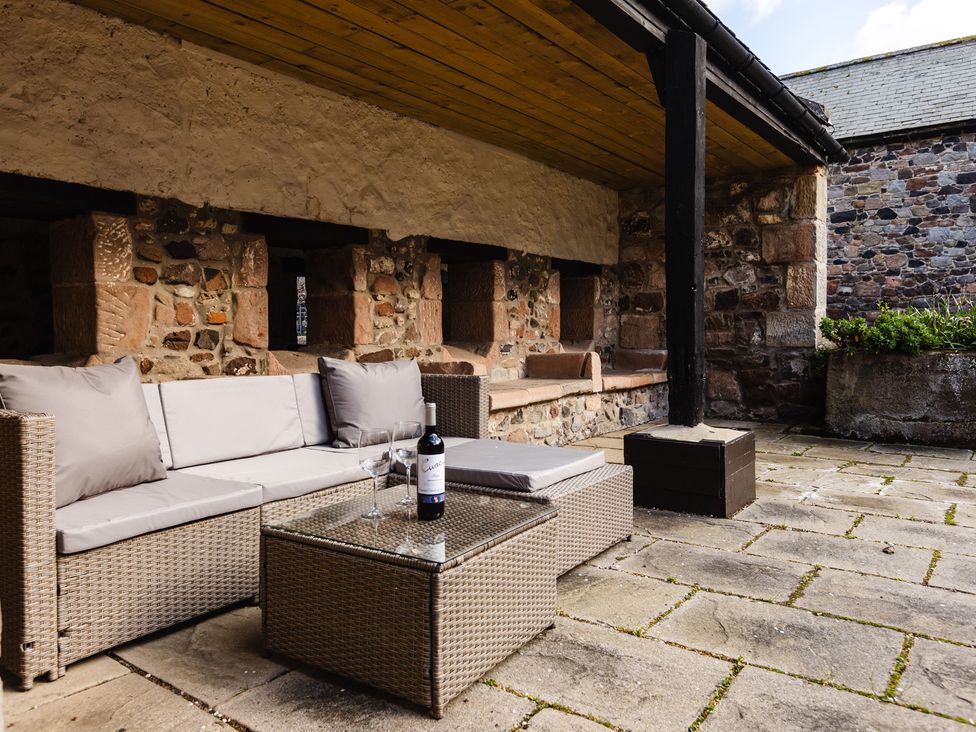 An outdoor seating area with a sofa and a glass table at Fern Cottage in Akeld near Wooler