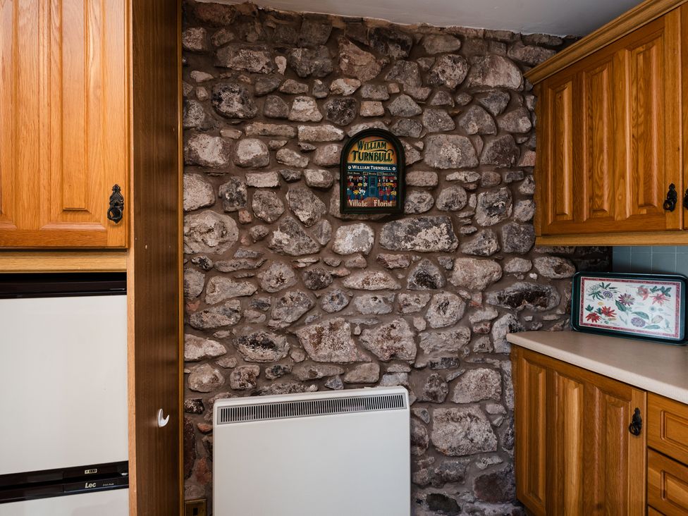 A kitchen with stone wall and wooden cabinets at Lupin Cottage in Akeld near Wooler
