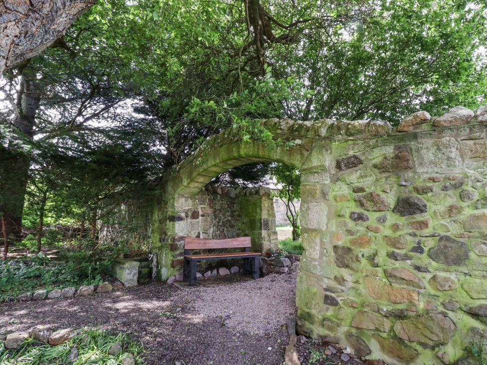 A garden with a stone archway and bench at Cherryburn Cottage in Akeld near Wooler