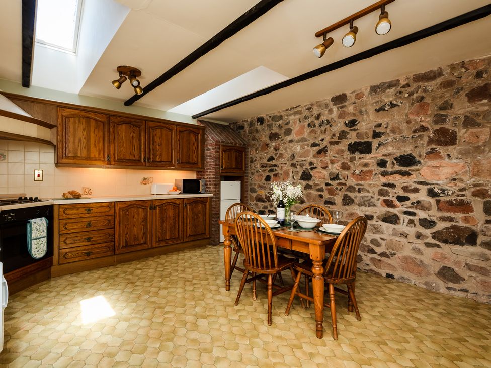 A kitchen with wooden cabinets and a dining table at Bramble Cottage in Akeld near Wooler