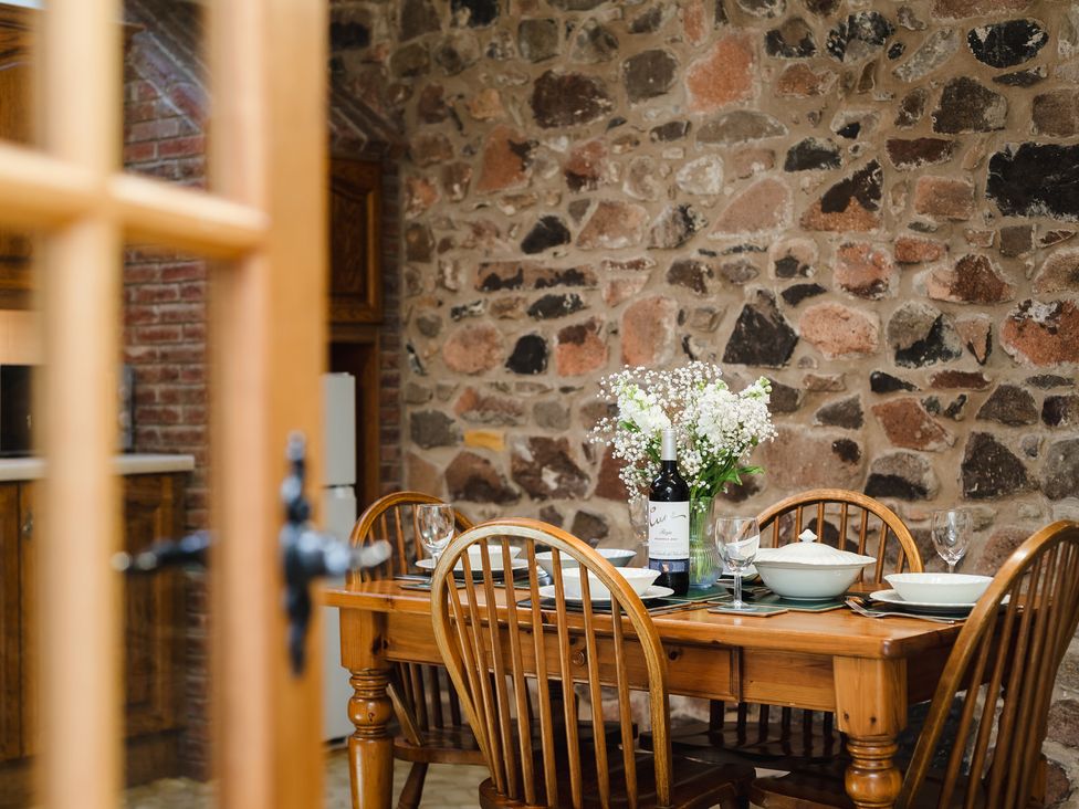 A dining room with a wooden table and flower vase at Bramble Cottage in Akeld near Wooler