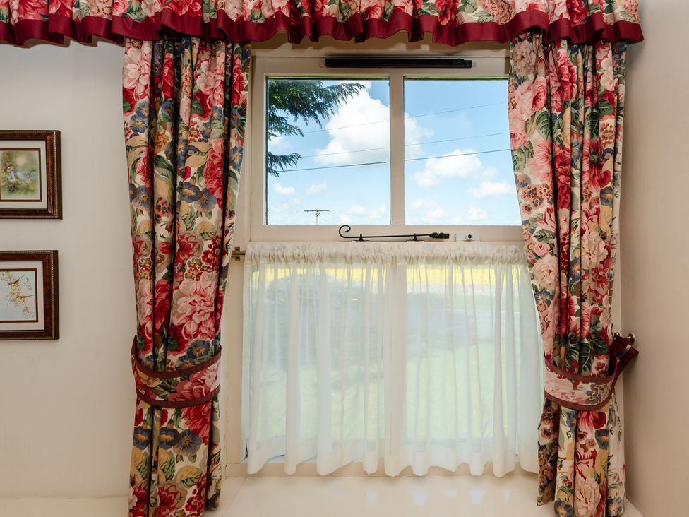 A window with floral curtains and framed pictures at Bramble Cottage Akeld near Wooler