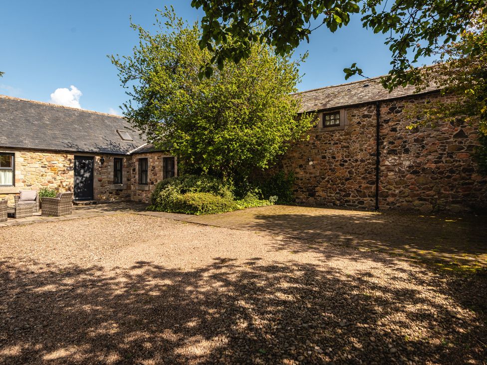 An outdoor area with a stone building and a gravel driveway at Bramble Cottage in Akeld near Wooler