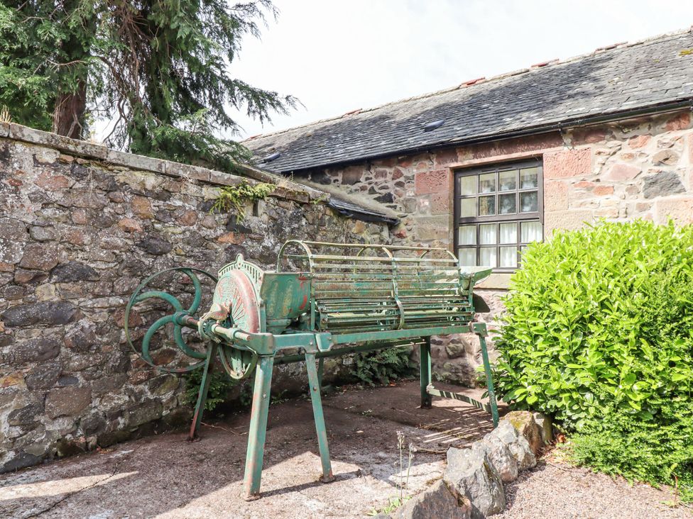 An outdoor area with a stone wall, window, green bush, and farm equipment at Hollyhock in Akeld near Wooler