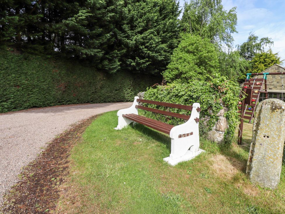 A bench along a path with grass and trees at Hollyhock in Akeld near Wooler