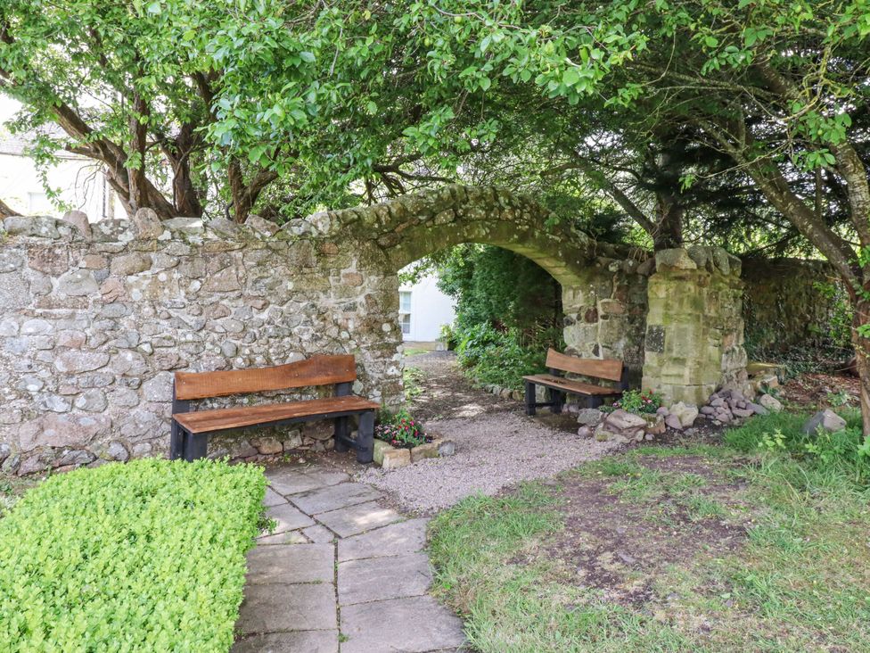 A garden with stone walls and wooden benches at Hollyhock in Akeld near Wooler