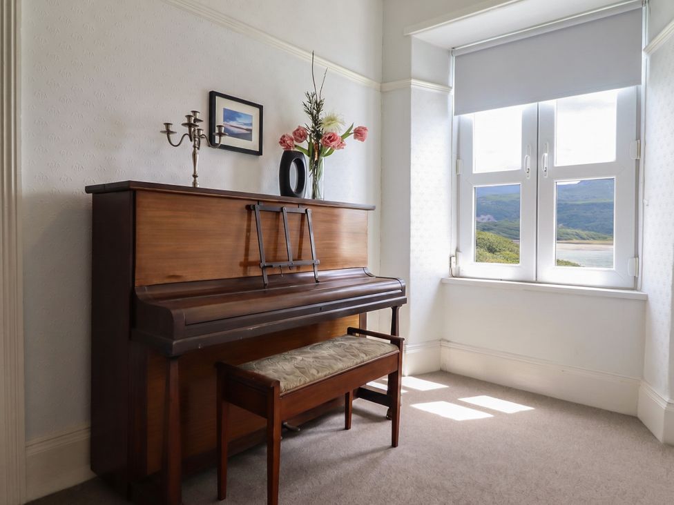 A music room with a piano and bench at 5 Porkington Terrace in Barmouth