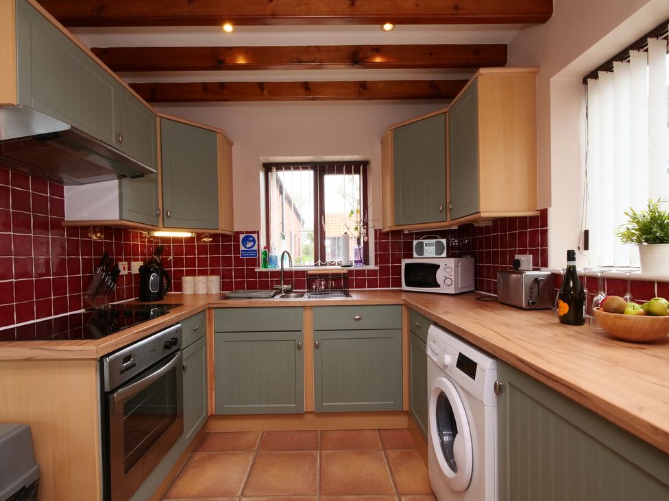 A kitchen with cabinets, stove, microwave, and washing machine at Scoresby Cottage @ Summerfield Farm, Hawsker
