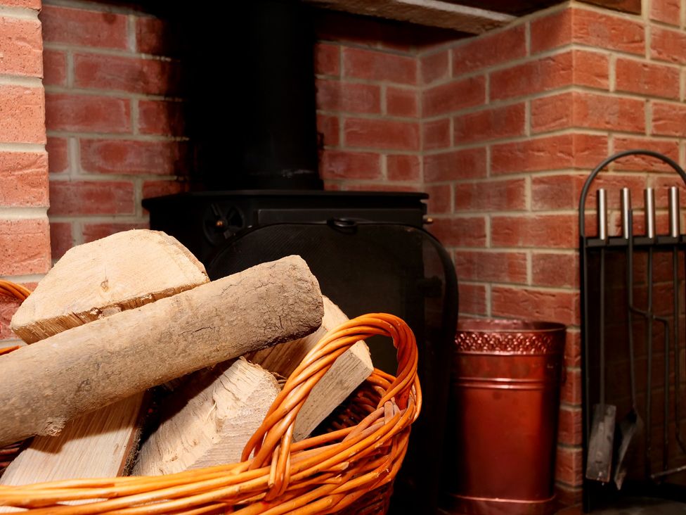 A living room with a fireplace and a basket of logs at Scoresby Cottage @ Summerfield Farm, Hawsker