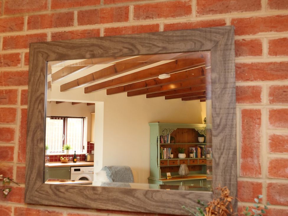 A mirror reflecting a living room with furniture and shelves at Scoresby Cottage @ Summerfield Farm, Hawsker