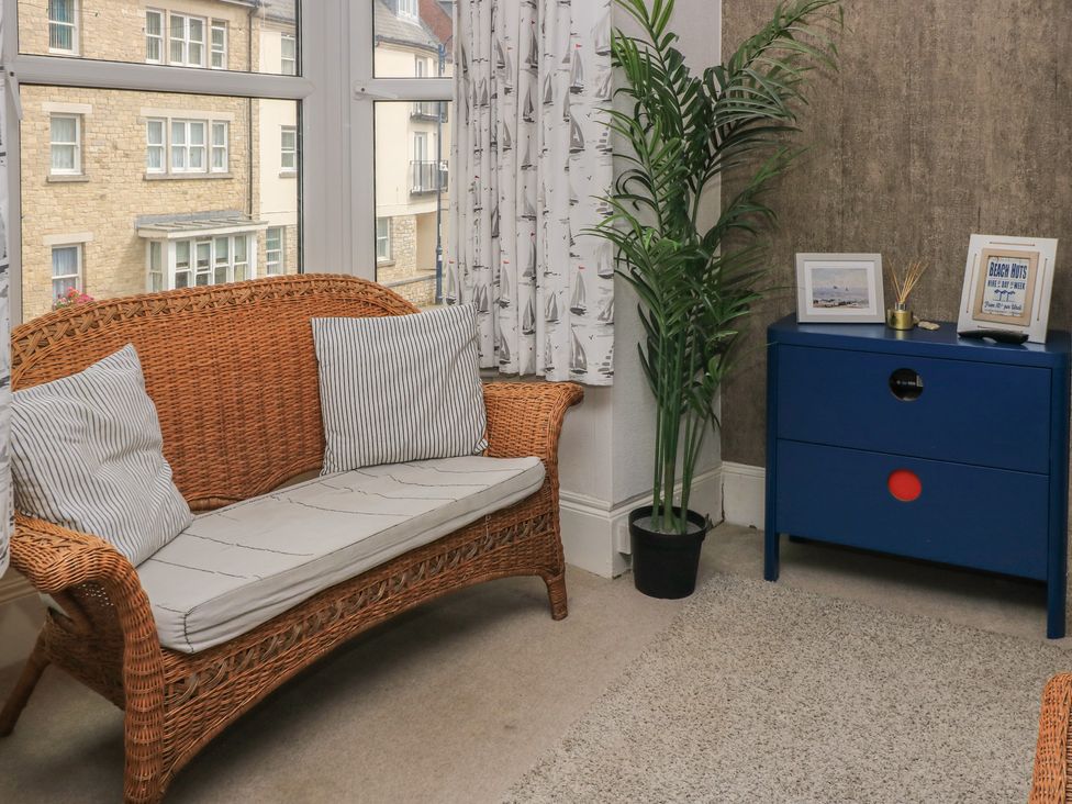 A living room with a wicker sofa and blue drawer unit at Still Waters in Swanage